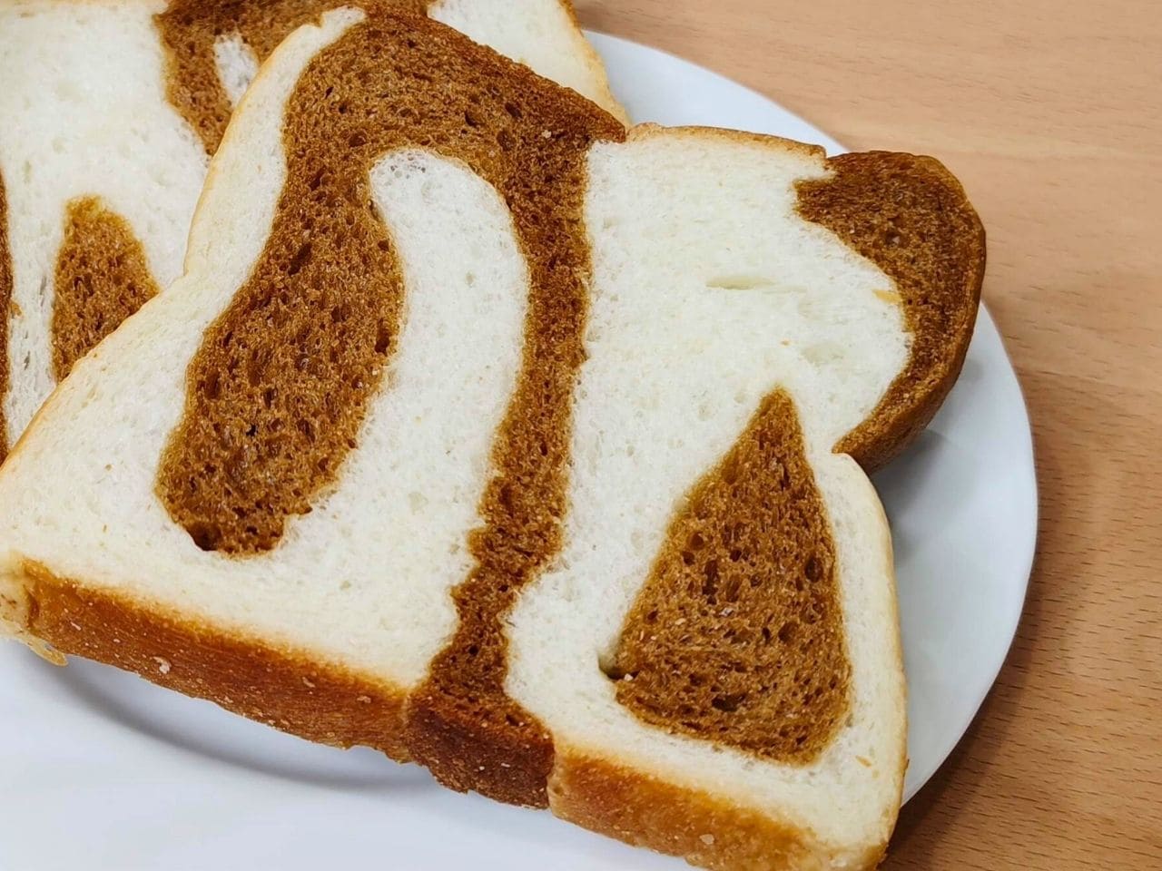 お皿にのせたマーブル食パン2枚の断面のアップ。黒糖生地が白い生地の中で大きくうねっている | アレルギー対応パンのtonton
